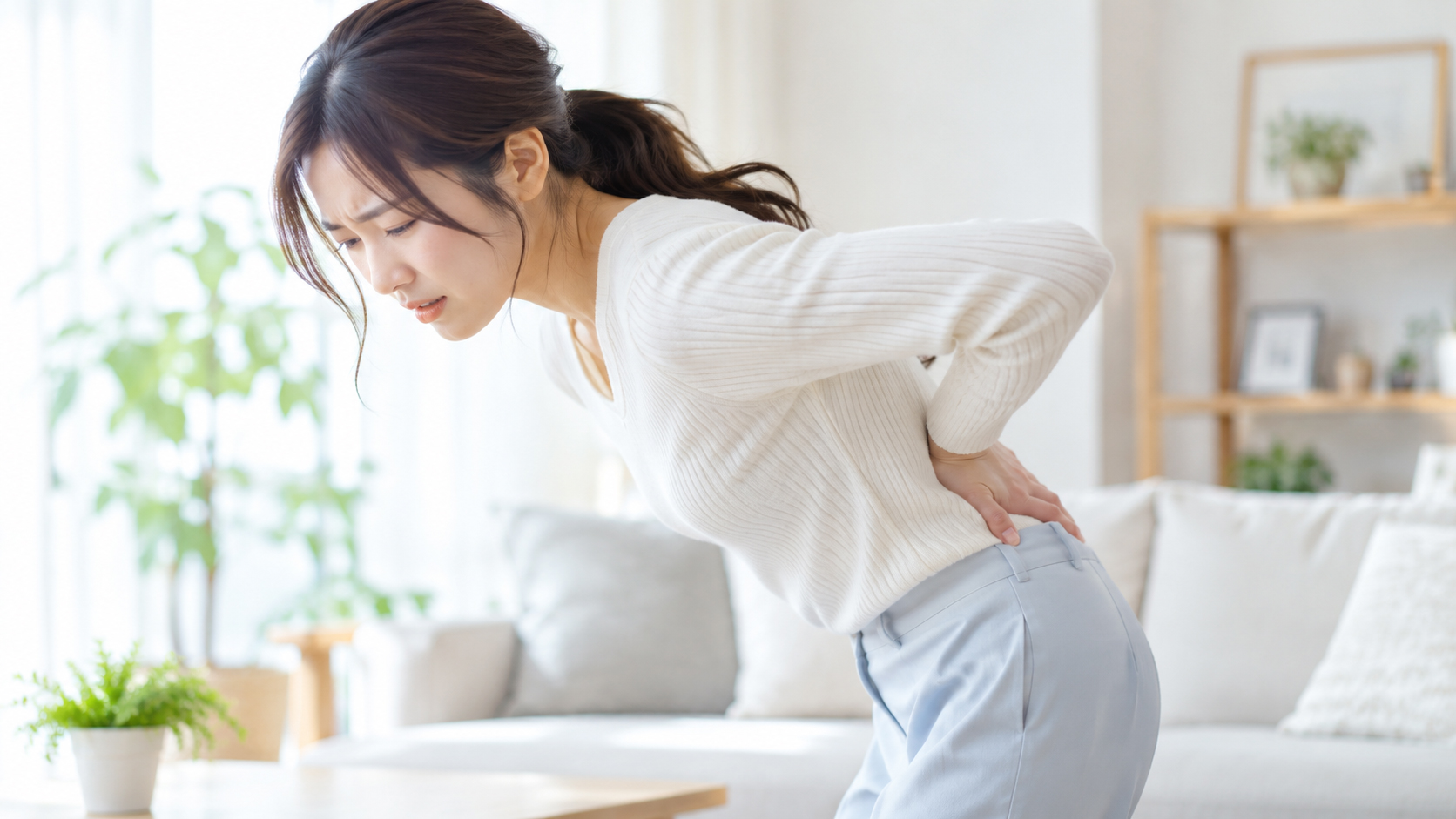 明るいリビングで腰の痛みに悩む女性のイメージ